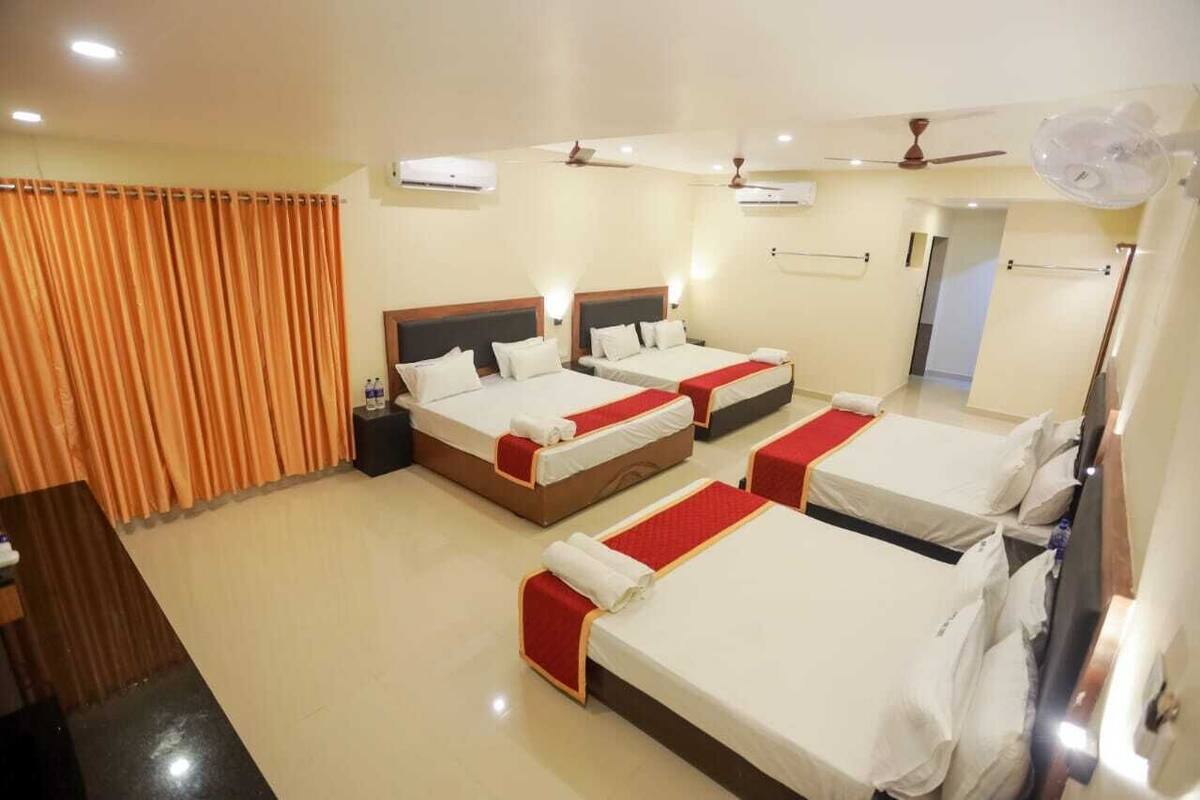 A hotel room with three beds, a wooden desk, and a large window with curtains.