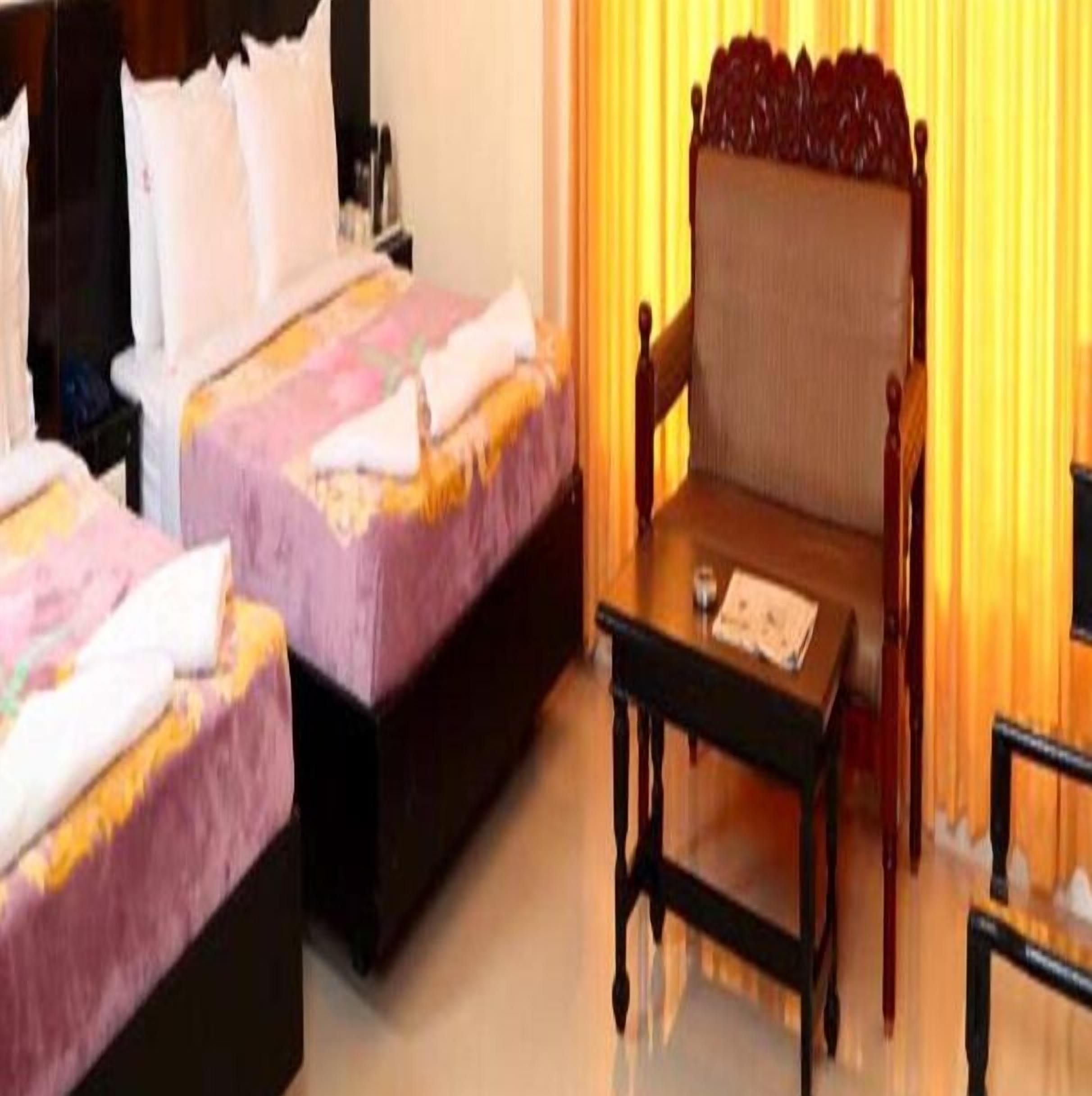 Una habitación de hotel con dos camas, una silla de madera y una mesita.