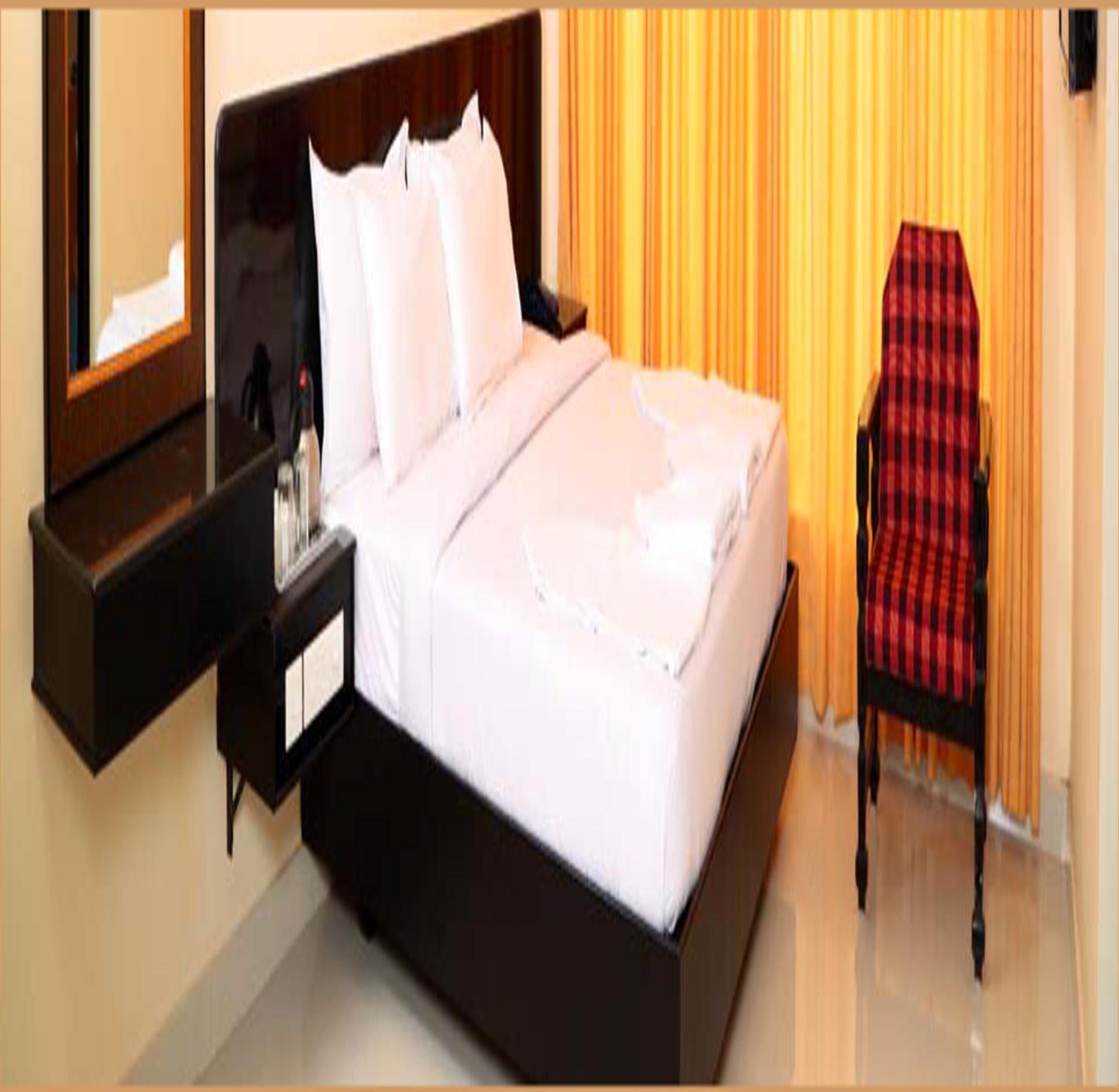 A hotel room with a bed, a nightstand, a chair, and a window with curtains.