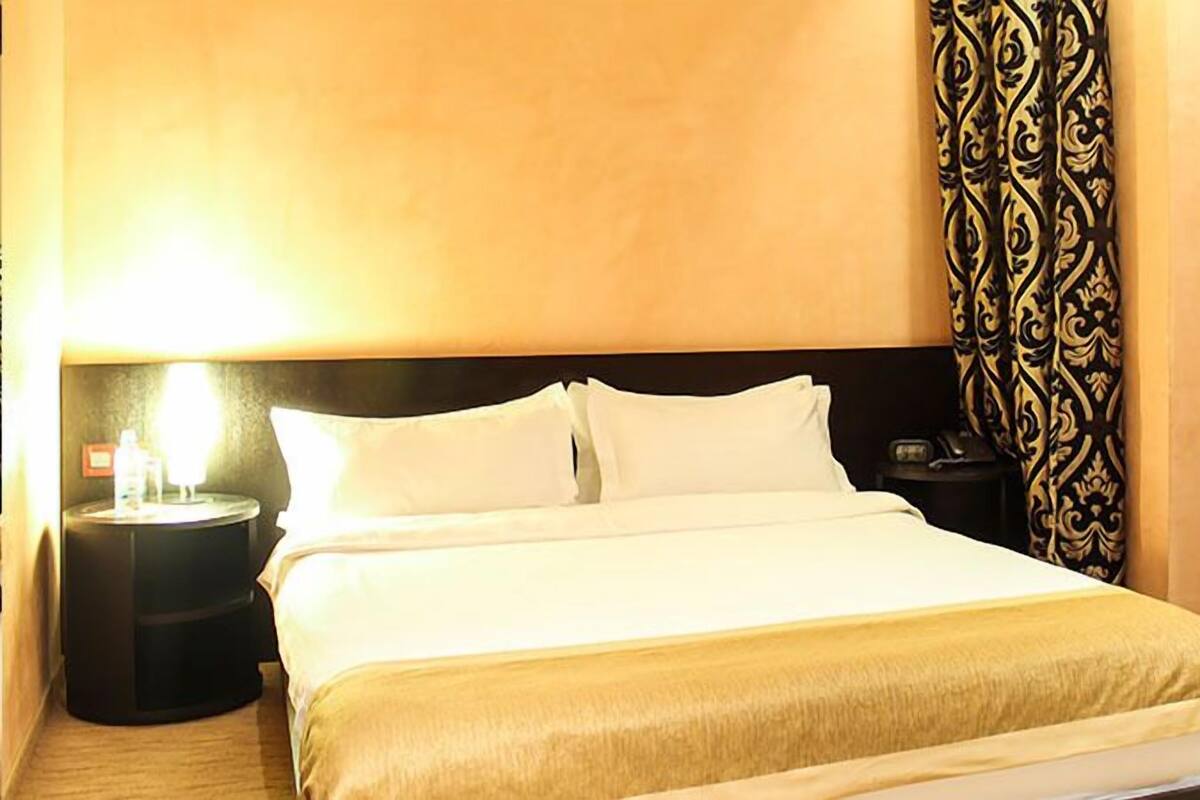 Una habitación de hotel con cama, mesita de noche, lámpara y cortina estampada.