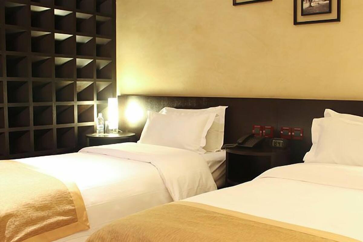 Una habitación de hotel con dos camas, una mesita de noche con una lámpara y un teléfono en la pared.