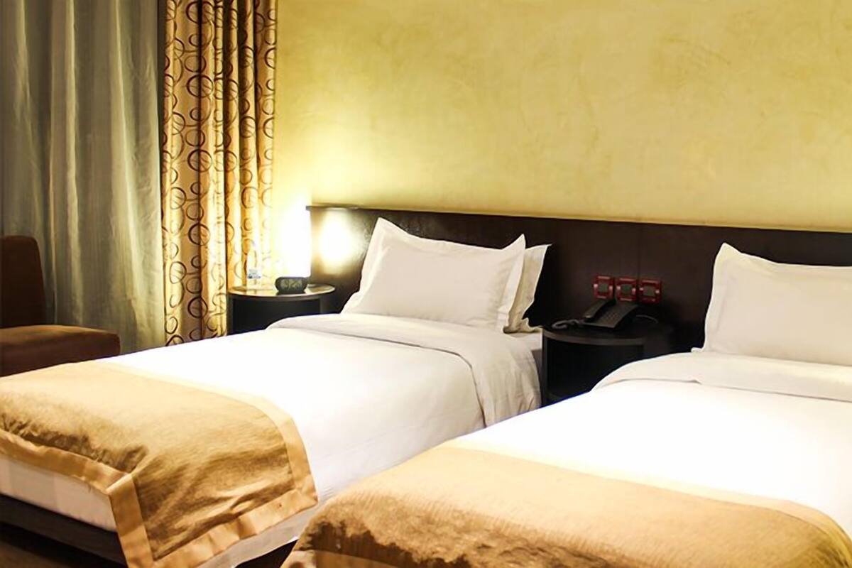 Una habitación de hotel con dos camas, una mesita de noche con lámpara y una silla.