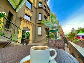 Ein Café mit einer Kaffeetasse auf einem Tisch, ein Gebäude mit einer grünen Markise und eine Treppe, die zum Eingang führt.