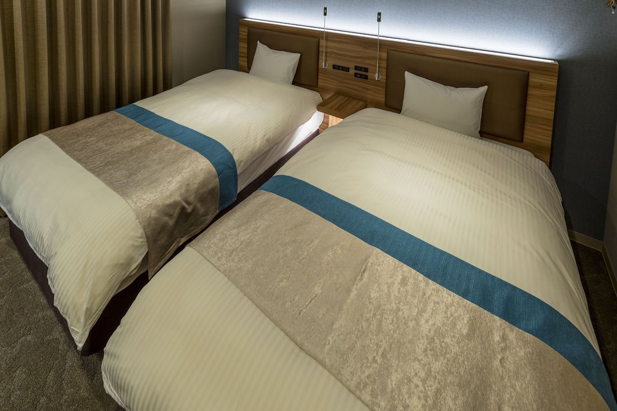 A hotel room with two beds, each with a headboard and a bedside table.