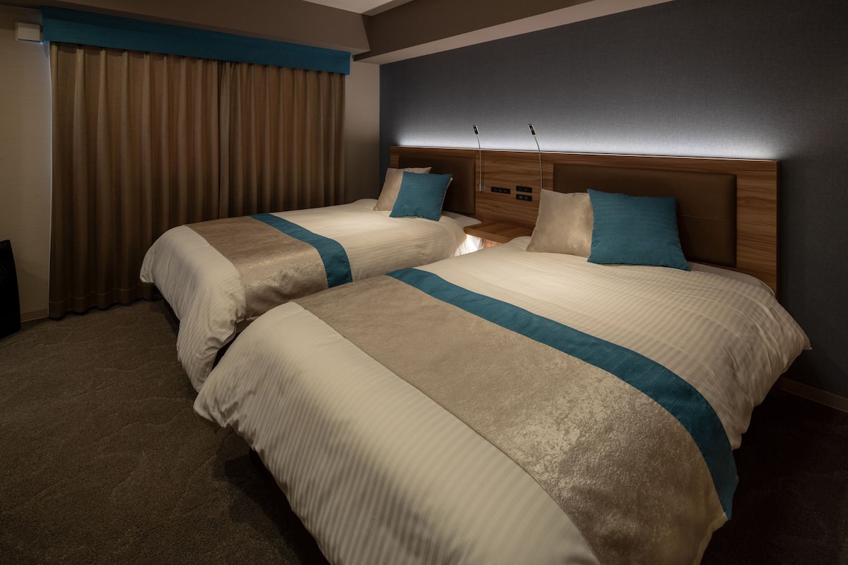 A hotel room with two beds, a wooden headboard, and a large window with curtains.