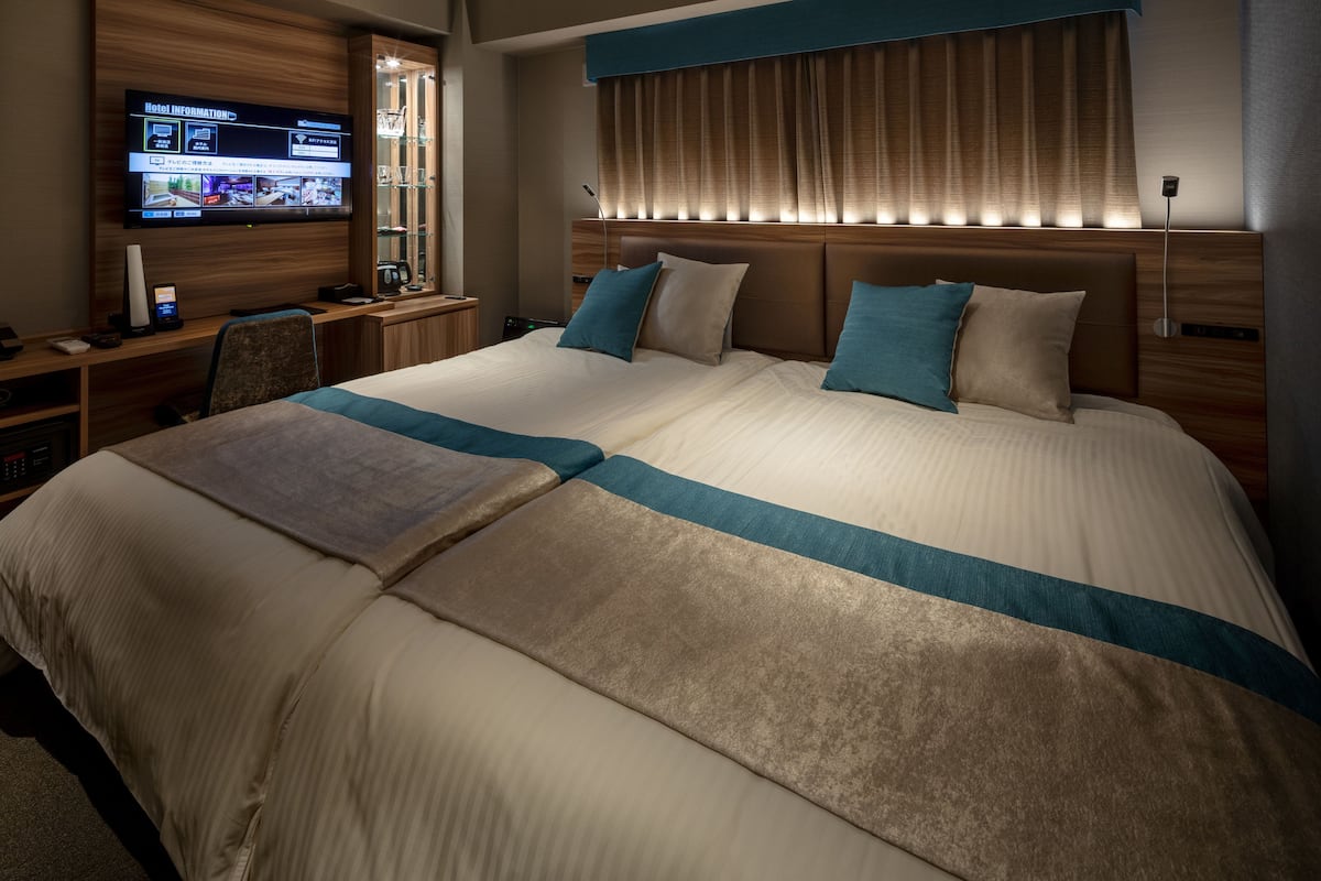 A hotel room with a large bed, a desk with a computer, and a TV displaying hotel information.