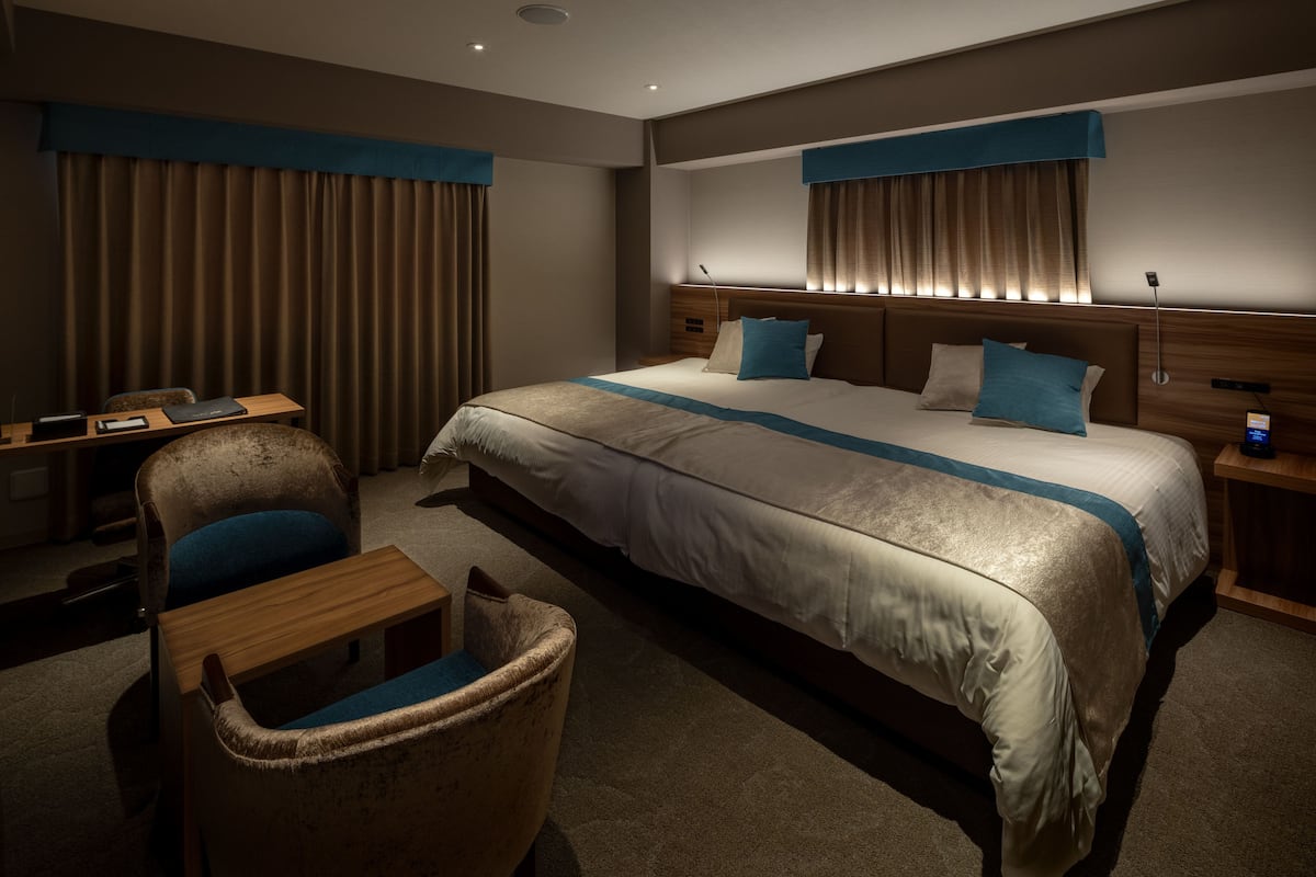 A hotel room with a large bed, a desk, a chair, and a nightstand.