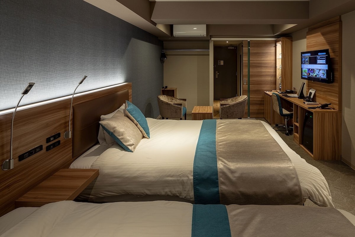 A hotel room with a bed, bedside tables, a desk, a TV, and a chair.