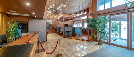 A spacious lobby with a wooden ceiling, a reception desk, and potted plants.