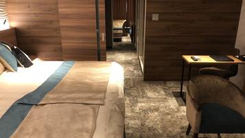 A hotel room with a large bed, a desk, and a chair. There is a wooden wall and a carpeted floor.