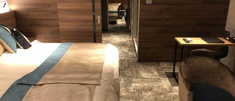 A hotel room with a large bed, a desk, and a chair. There is a wooden wall and a carpeted floor.