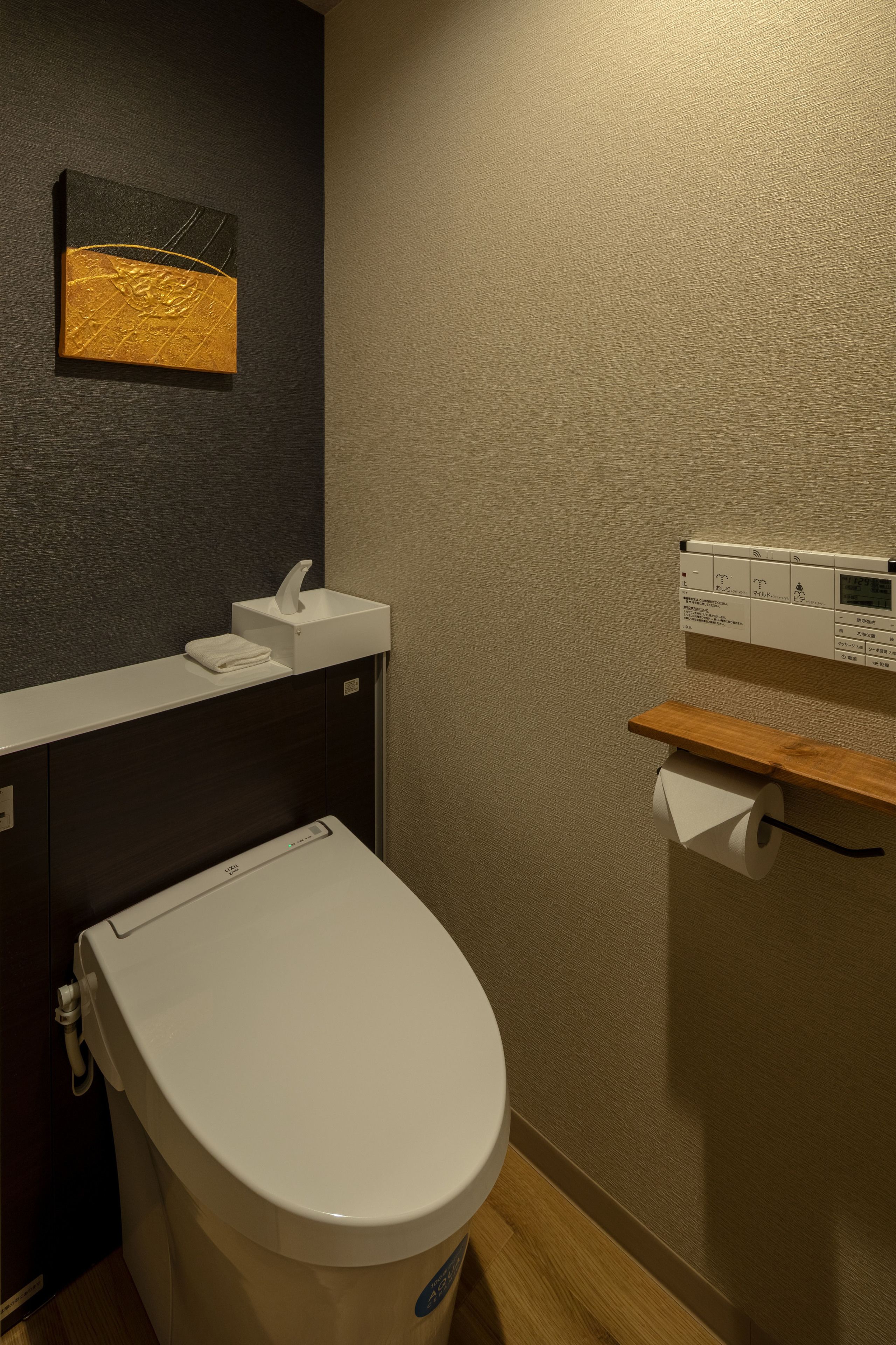 A modern bathroom with a toilet, sink, and a wall-mounted toilet paper dispenser.