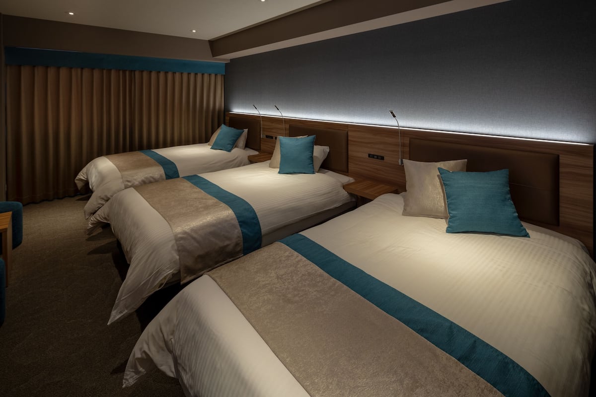 A hotel room with three beds, each with a headboard, and a large window with curtains.