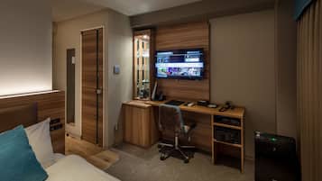 A hotel room with a bed, a desk with a computer, a TV mounted on the wall, and a small cabinet.