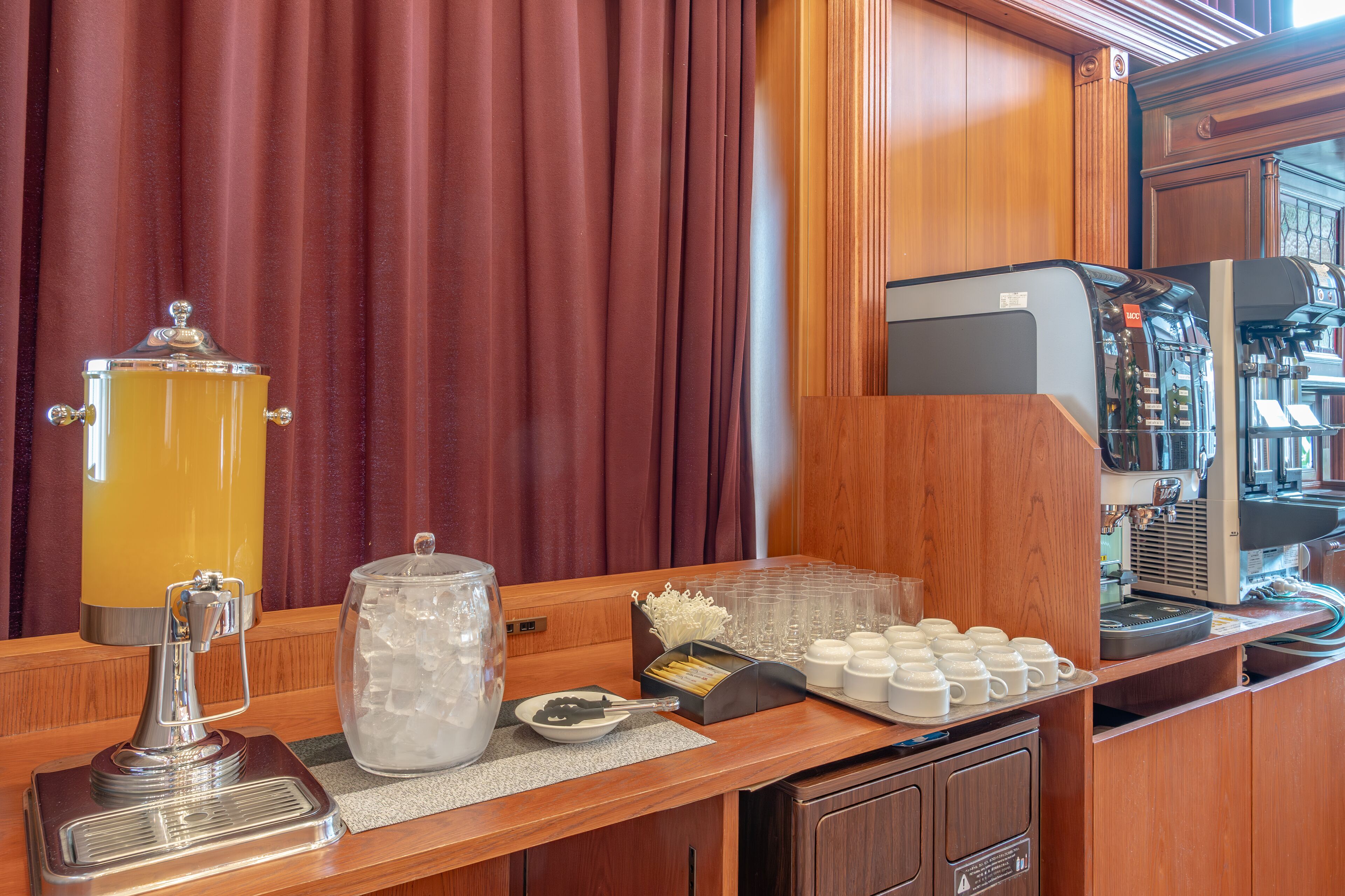 Una estación de café con una máquina de café, un dispensador amarillo grande para bebidas y una bandeja de tazas blancas.