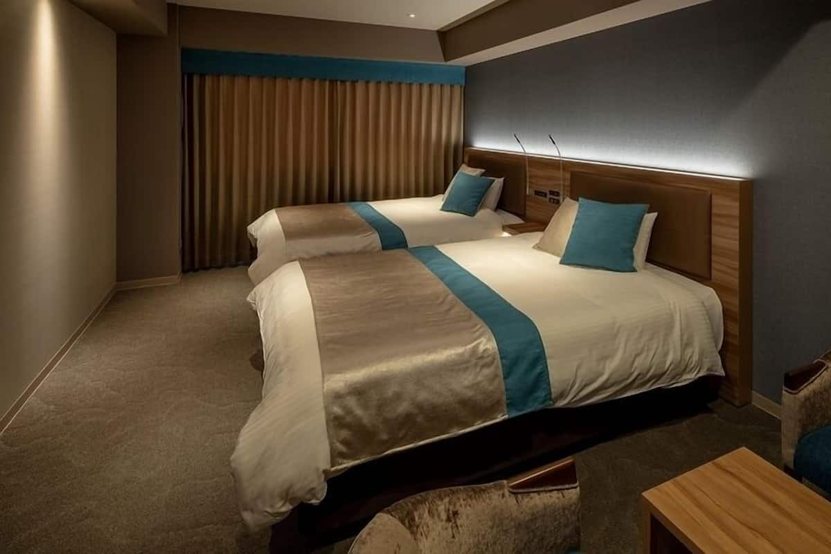 A hotel room with two beds, a wooden headboard, a desk, and a chair.