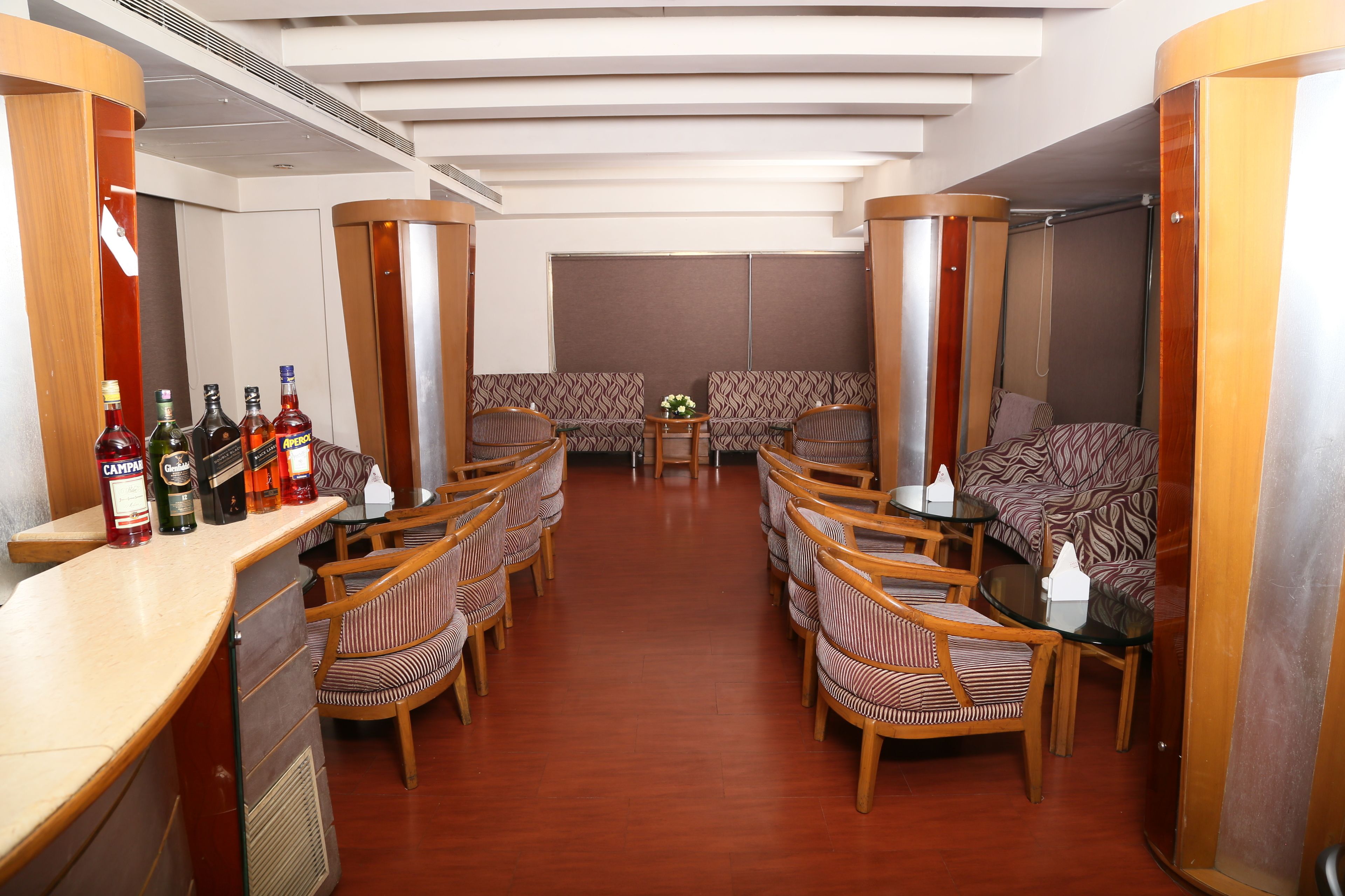 A compact, well-lit room with a bar area on one side, seating arrangements, and a small table with a vase of flowers.
