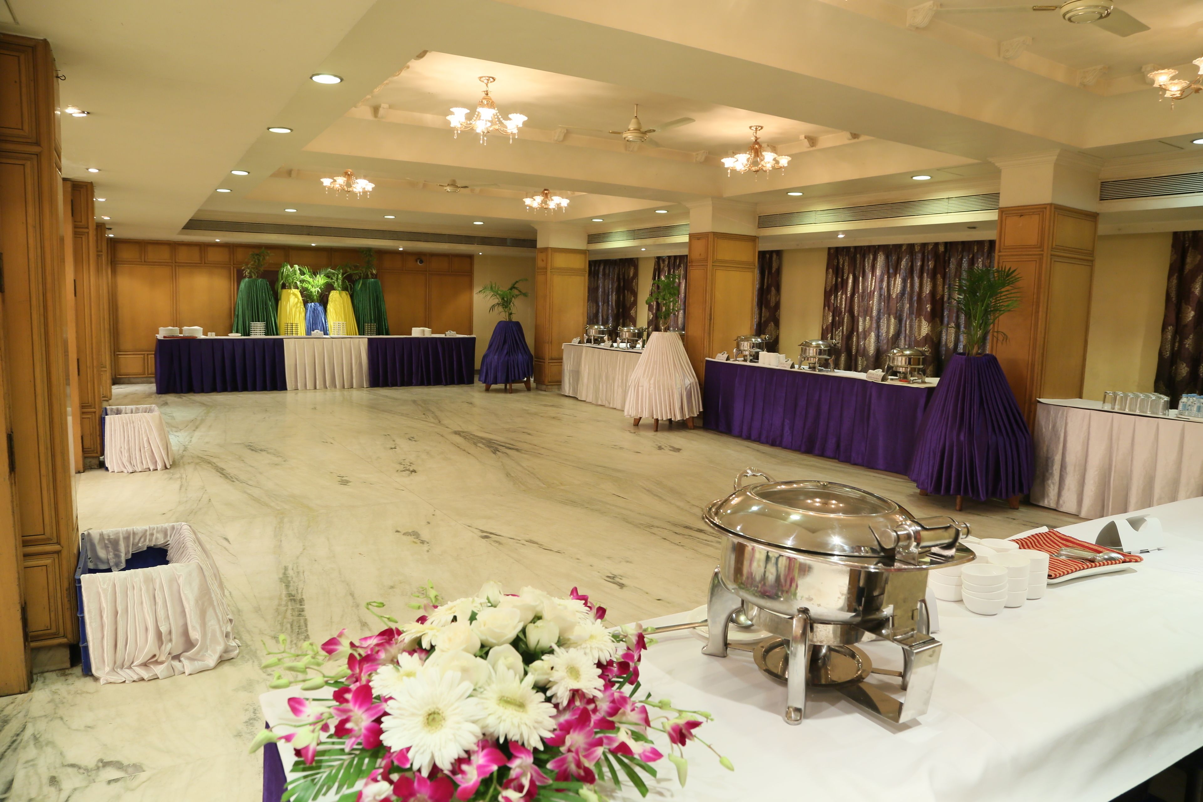Une salle de banquet avec des tables recouvertes de nappes, un buffet et des compositions florales.