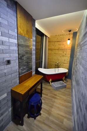 A narrow bathroom with a wooden bench, a red bathtub, and a blue stool.
