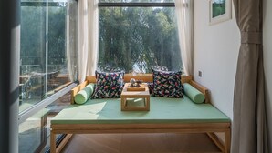 A cozy room with a green sofa, patterned cushions, a wooden coffee table, and large windows offering a view of trees. - CTN LiRiver Boutique Hotel (Guilin)
