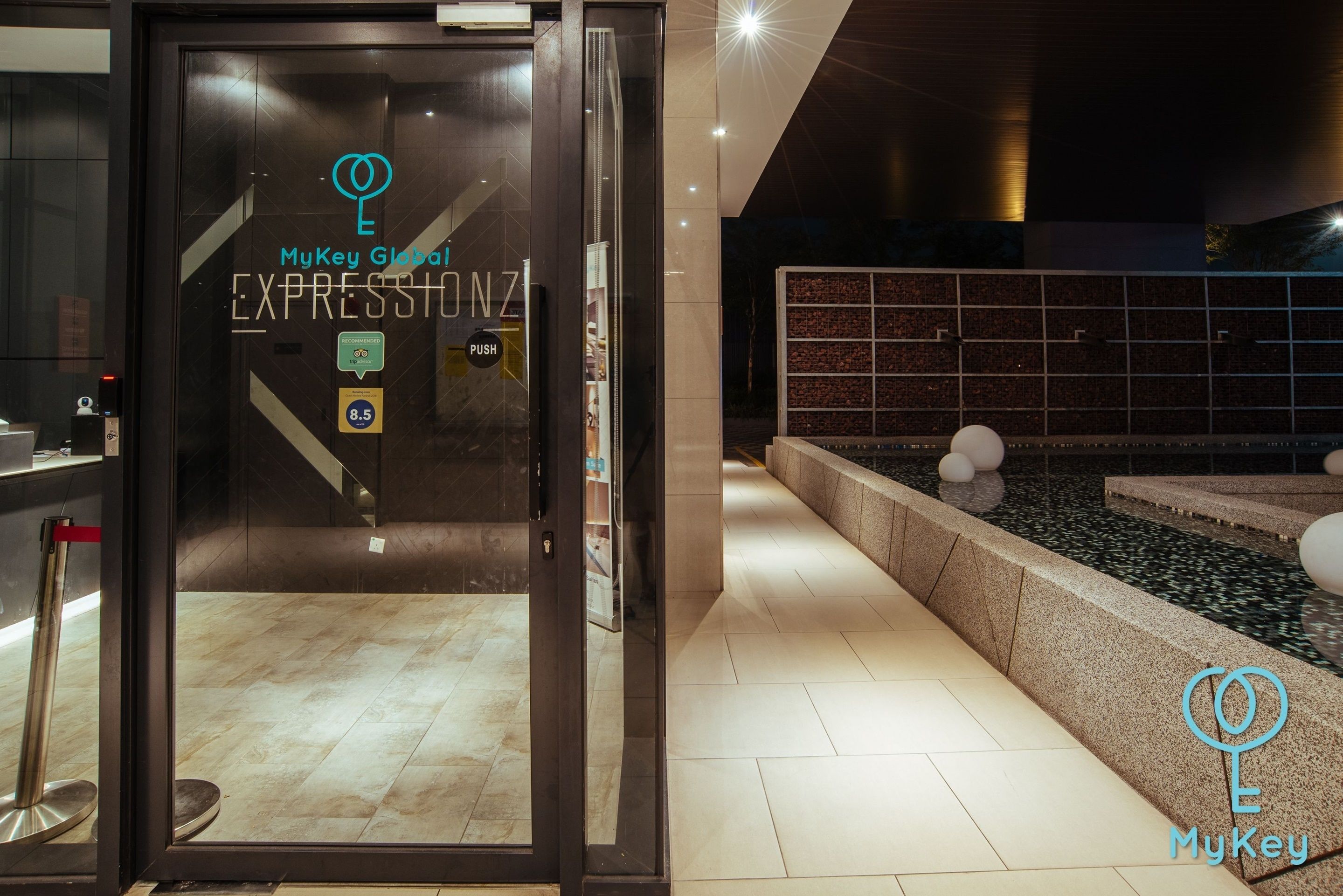 Ein Hotel mit Eingang, Glasdoor, Rezeption und einer Sitzecke mit Wasserspiel.