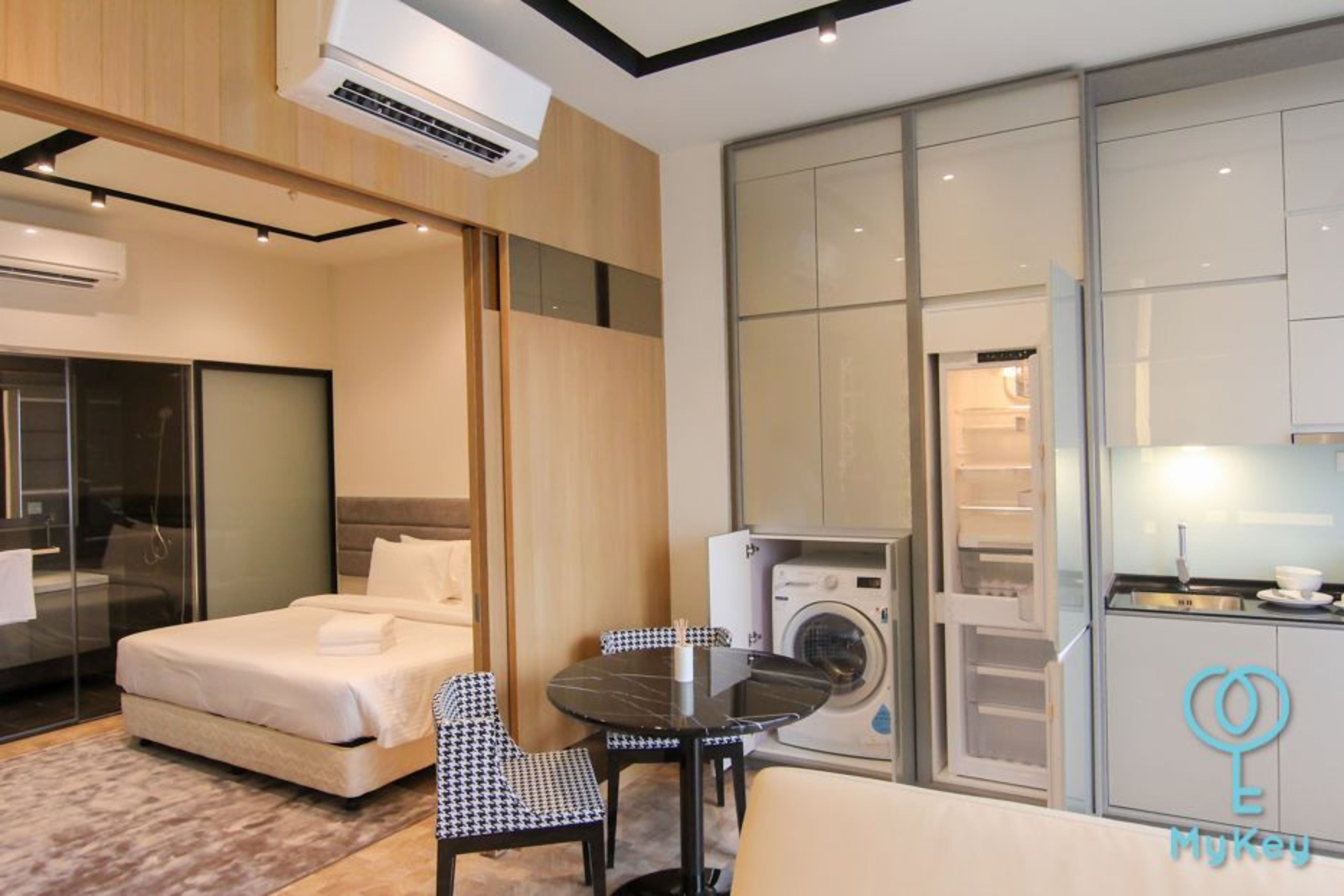Ein modernes Hotelzimmer mit Bett, Esstisch, Stühlen, einer Waschmaschine und einer Küchenzeile.