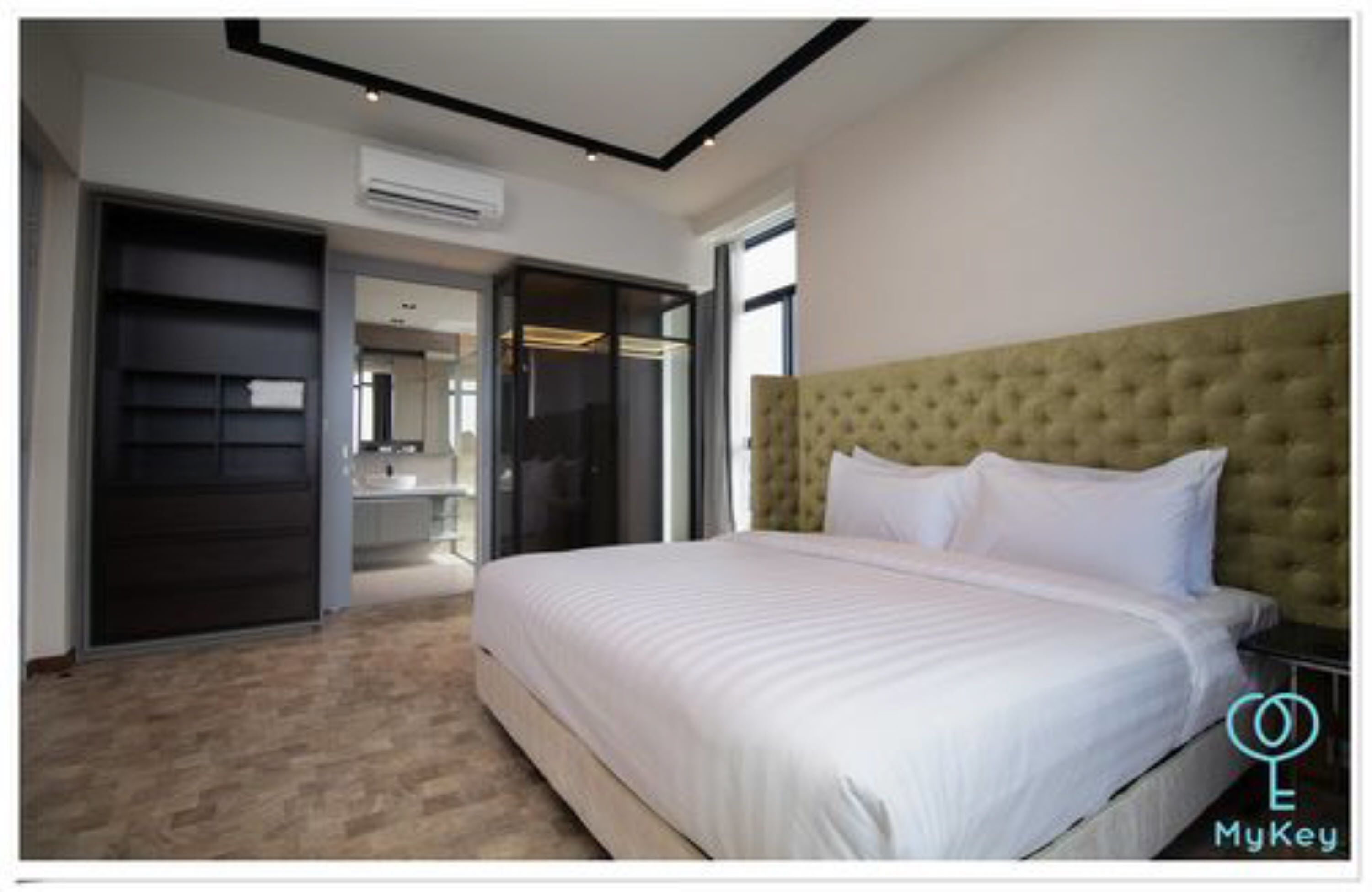A modern bedroom with a large bed, a tufted headboard, and a sliding glass door leading to a bathroom.