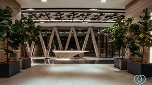 Eine moderne Lobby mit einer Rezeption mit dem Namen "Expressionz", umgeben von Topfpflanzen und einem geometrischen Deckenstil.