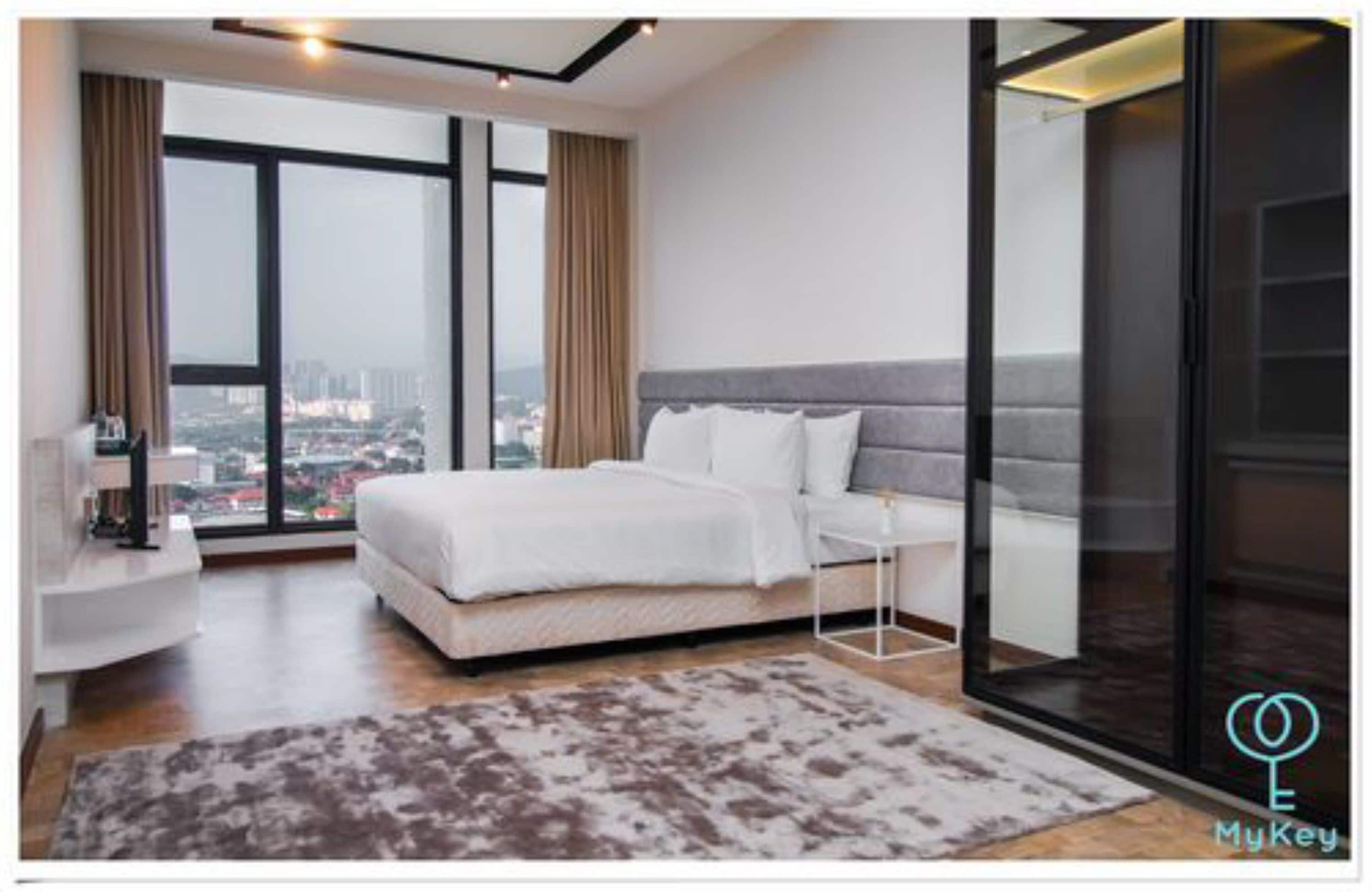 Una habitación de hotel moderna con una cama grande, una mesita de noche, un separador de vidrio y vistas a la ciudad.