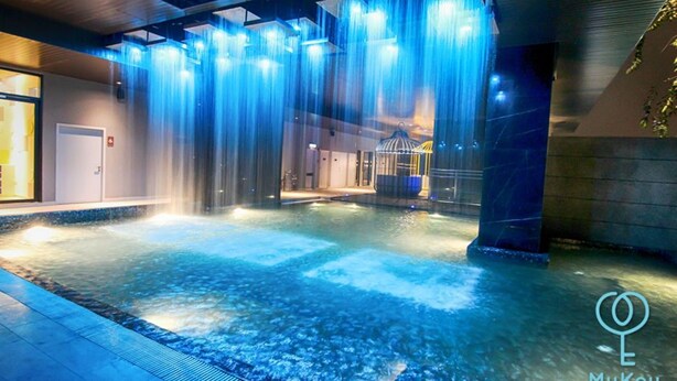 Ein moderner Innenpool mit verschiedenen Wasserspielen, darunter Wasserfälle und eine zentrale Fontäne.