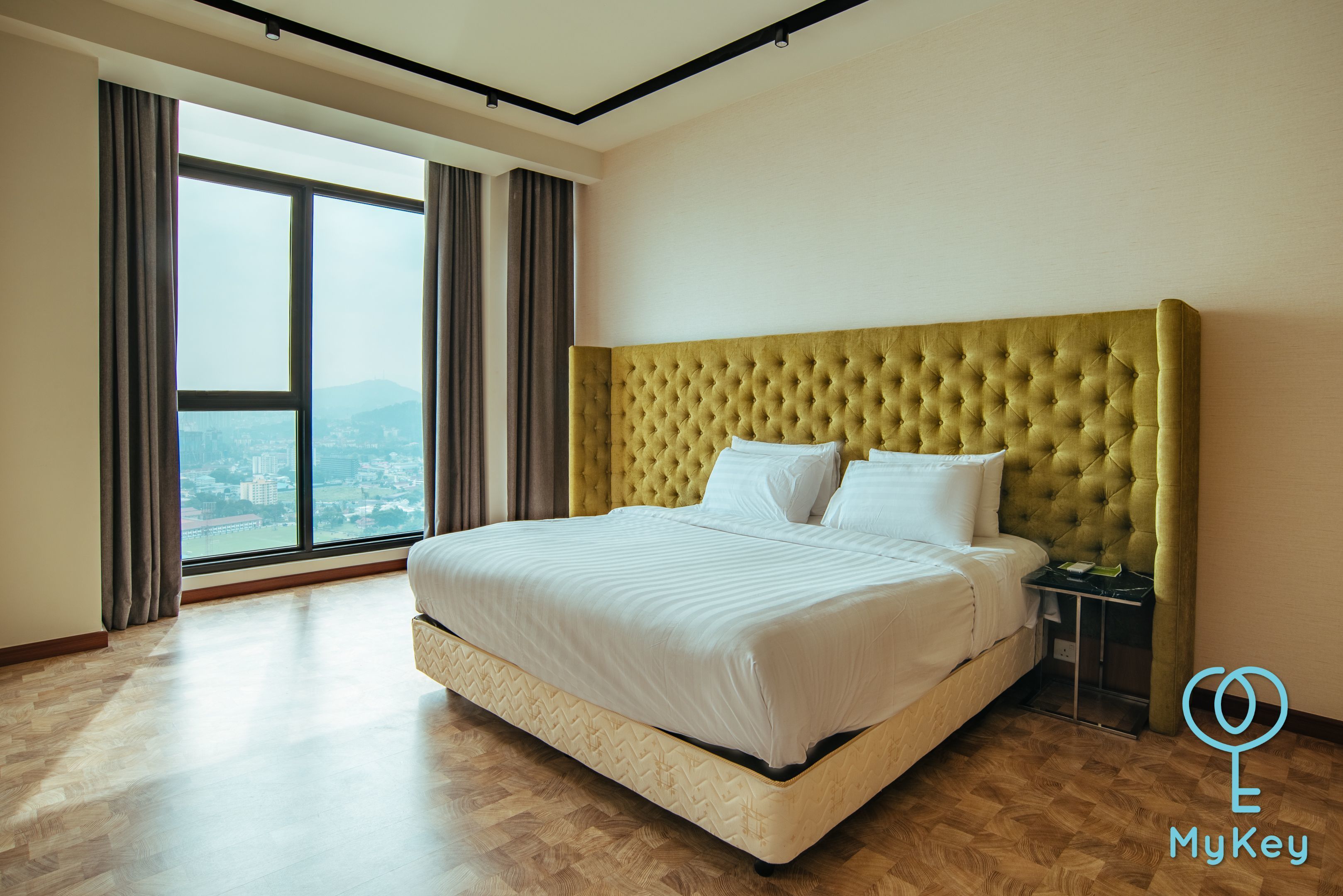 A modern hotel room with a large bed, a view of the city, and a green headboard.