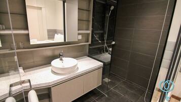 A modern bathroom with a round sink, a large mirror, and a shower area.