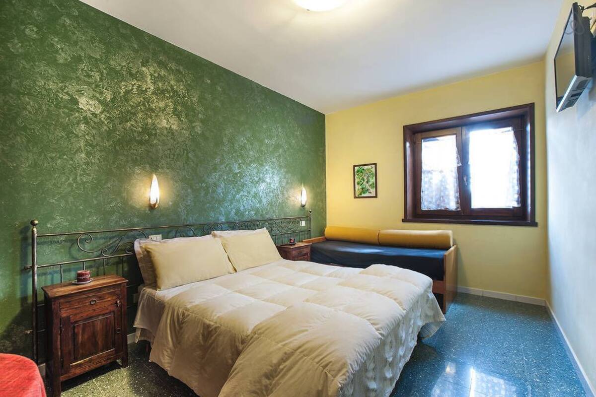 A bedroom with a bed, bedside tables, a nightstand, a window, and a wall-mounted TV.