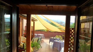 Un umbral abierto que da a un patio con mesas y sillas, un toldo amarillo y plantas en macetas.