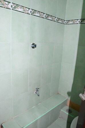 A bathroom with green tiles, a shower, a toilet, and a small bench.