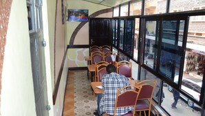 A restaurant with a row of wooden chairs and tables, a tiled floor, and large windows offering a view of the street outside. - Sir Kanja's Hotel (Nairobi)