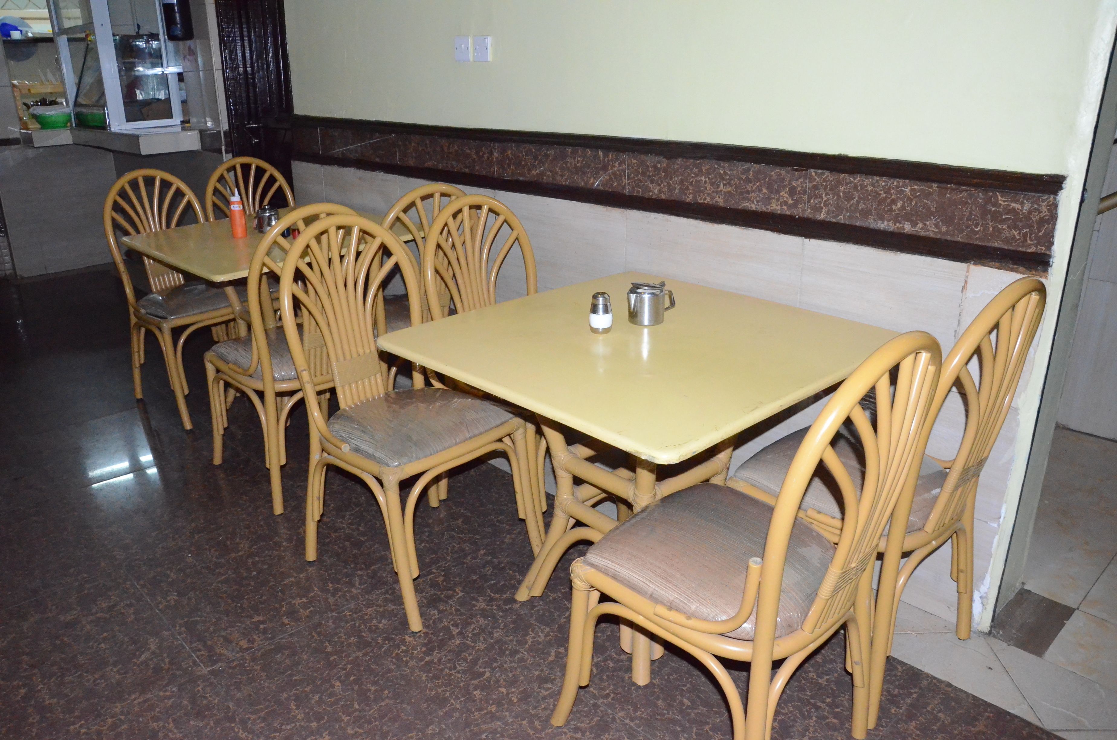 A dining area with a table and chairs, a tiled floor, and a wall with a brown baseboard.