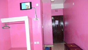 A pink-walled room with a white shelf, a small wooden table, and a door with a note on it. - Sir Kanja's Hotel (Nairobi)