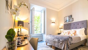 Quarto de hotel com cama, escrivaninha com luminária, cadeira e janela com vista para áreas verdes.