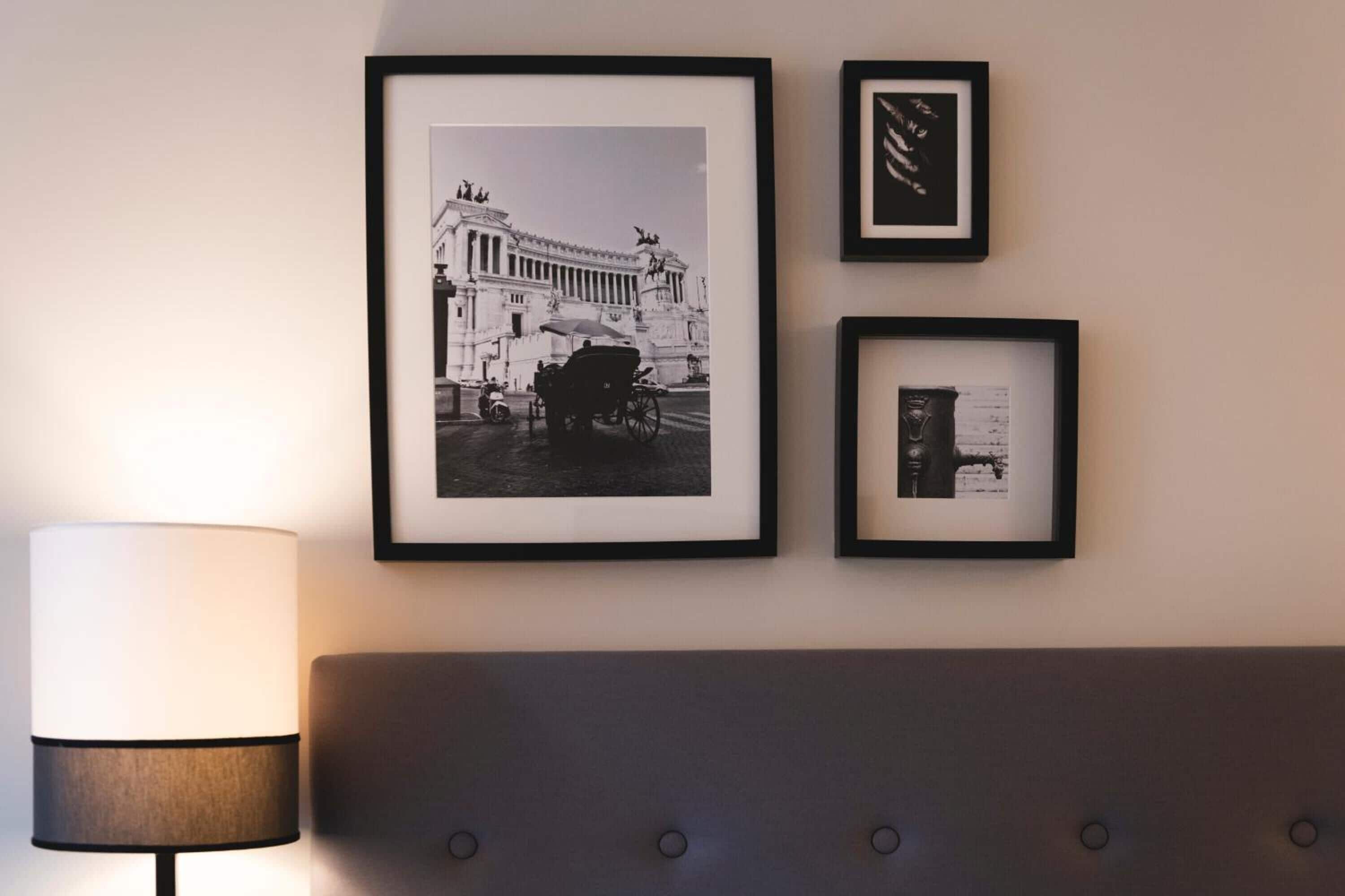 A framed photograph of a building with a horse-drawn carriage, a framed abstract artwork, and a framed document on a wall.