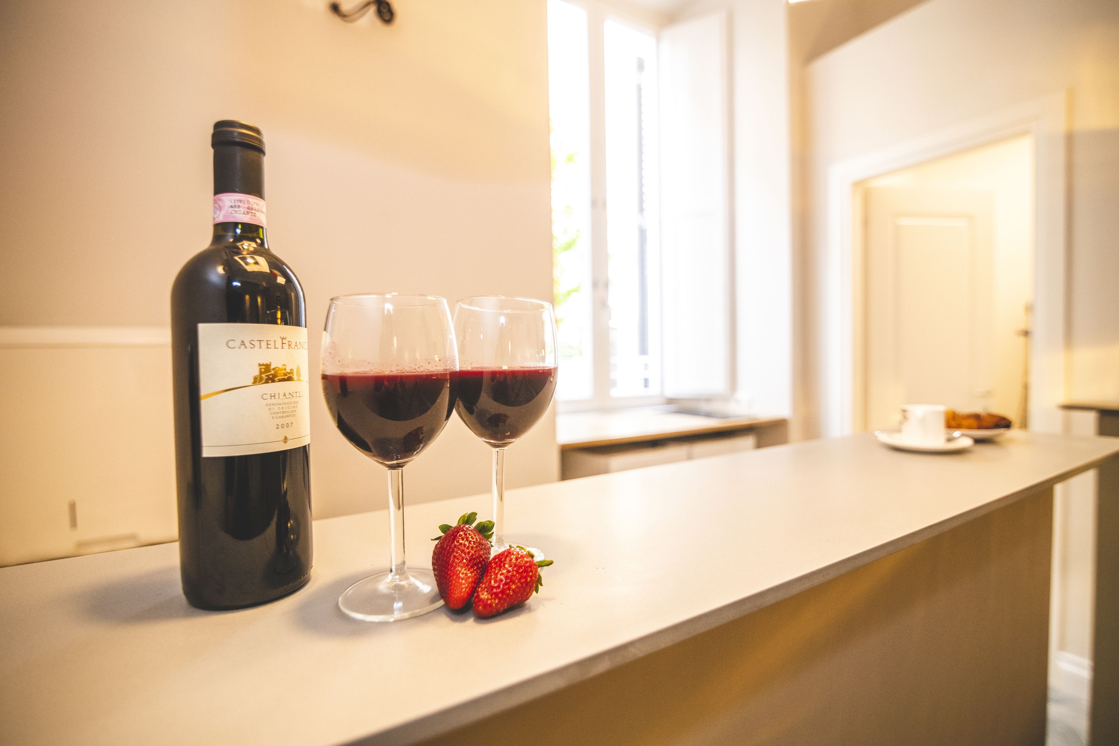 Uma garrafa de vinho Château Mouton Rothschild, duas taças de vinho tinto e duas morangos em uma bancada de cozinha.