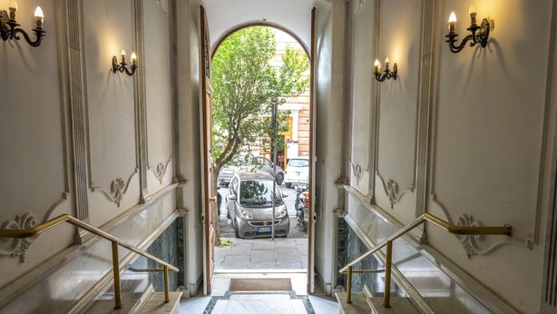 Uma escadaria imponente que dá para a rua, com castiçais decorados e uma vista livre de carros estacionados e árvores.