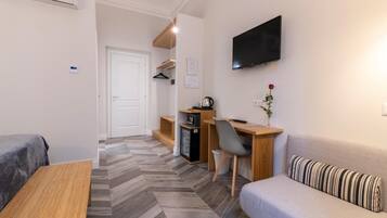 Une chambre d’hôtel moderne équipée d’un canapé, d’un petit bureau avec une chaise, d’une télévision et d’un coin cuisine.