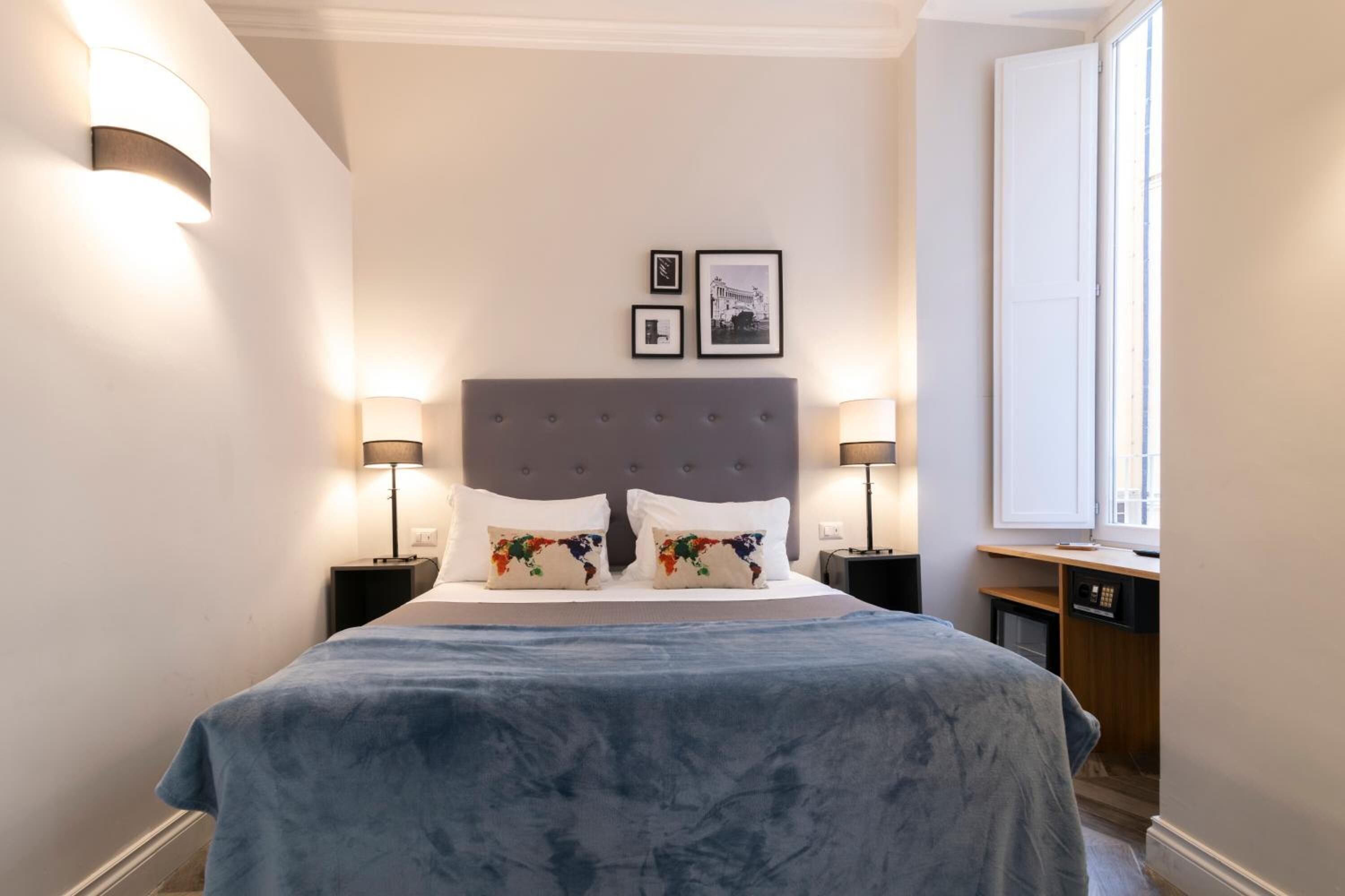 A neatly arranged bedroom with a large bed, two bedside tables with lamps, a window, and two framed pictures on the wall.