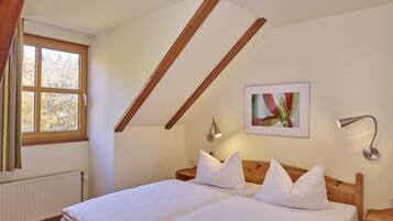 A bedroom with a wooden ceiling, a bed with white bedding, a window with a view of trees, and a framed picture on the wall.