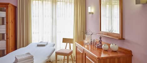 Une pièce comprenant un lit, une commode en bois, une chaise, un miroir et une fenêtre avec des rideaux.