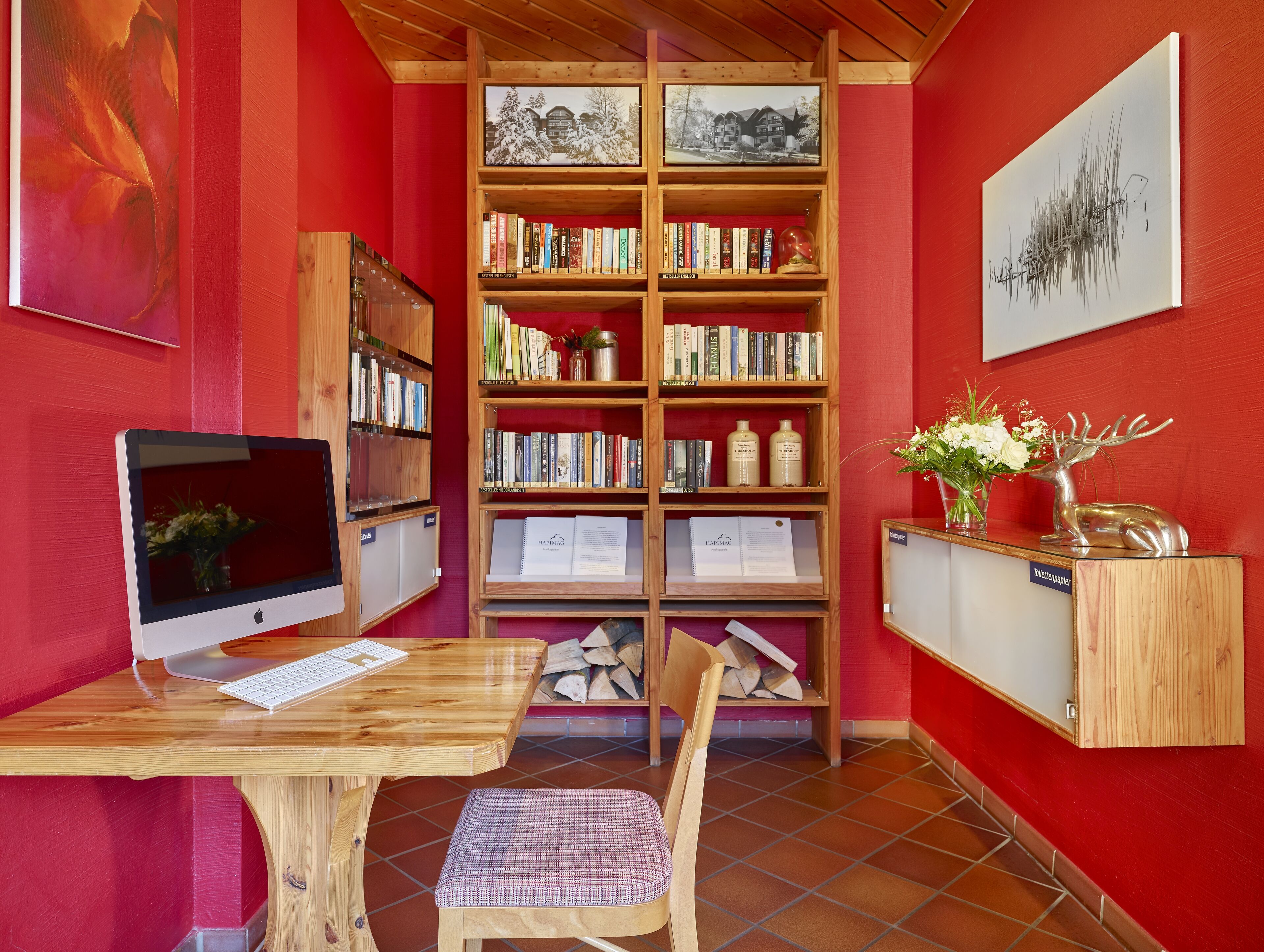 Un rincón acogedor para leer con un escritorio de madera, una computadora y una estantería llena de libros y adornos.