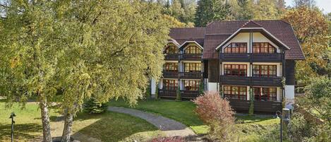 A traditional chalet-style building with multiple balconies and large windows, surrounded by a well-maintained garden with benches and a paved path.
