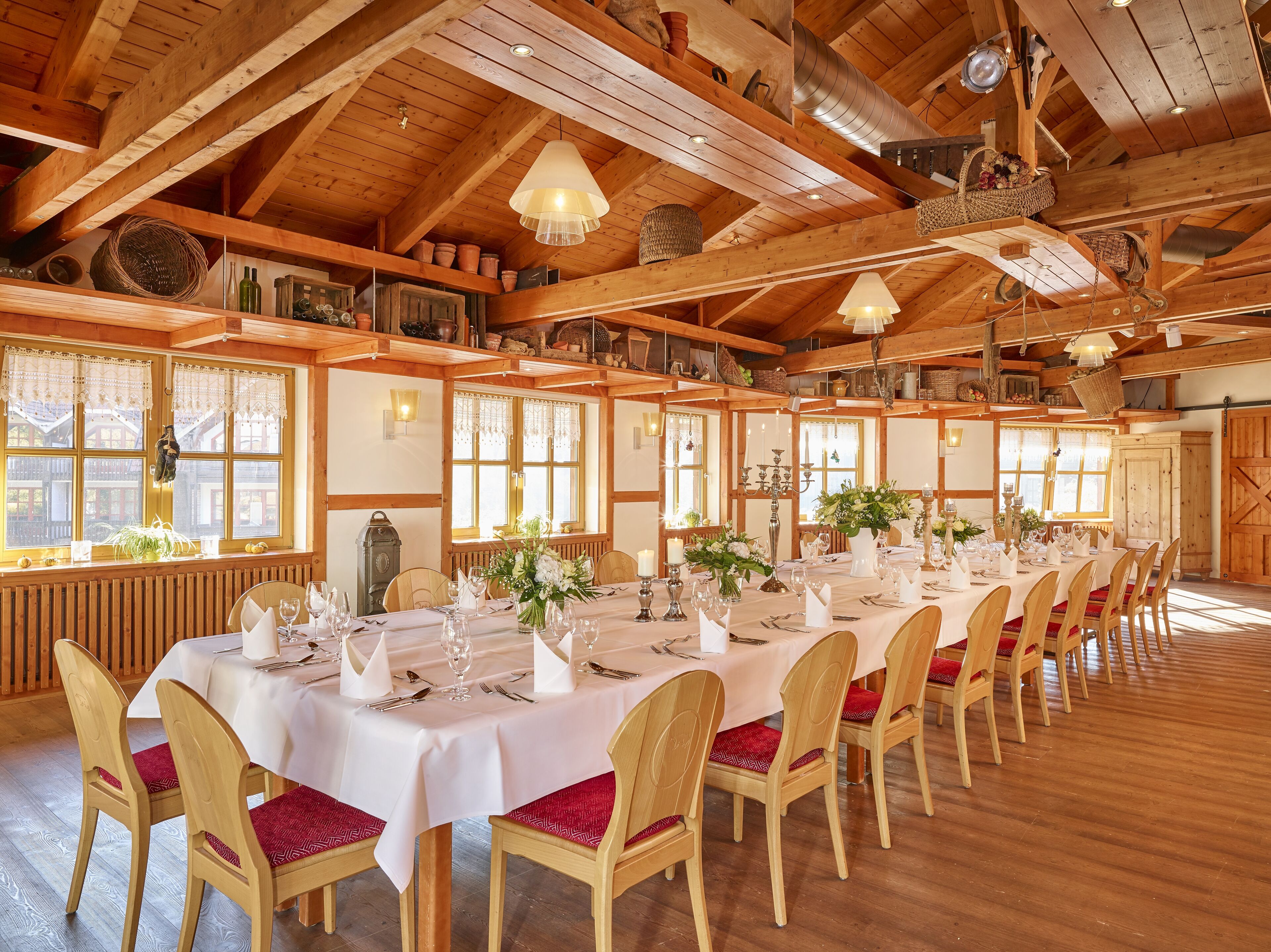 A long dining table set for a meal in a wooden interior with high ceilings and large windows.