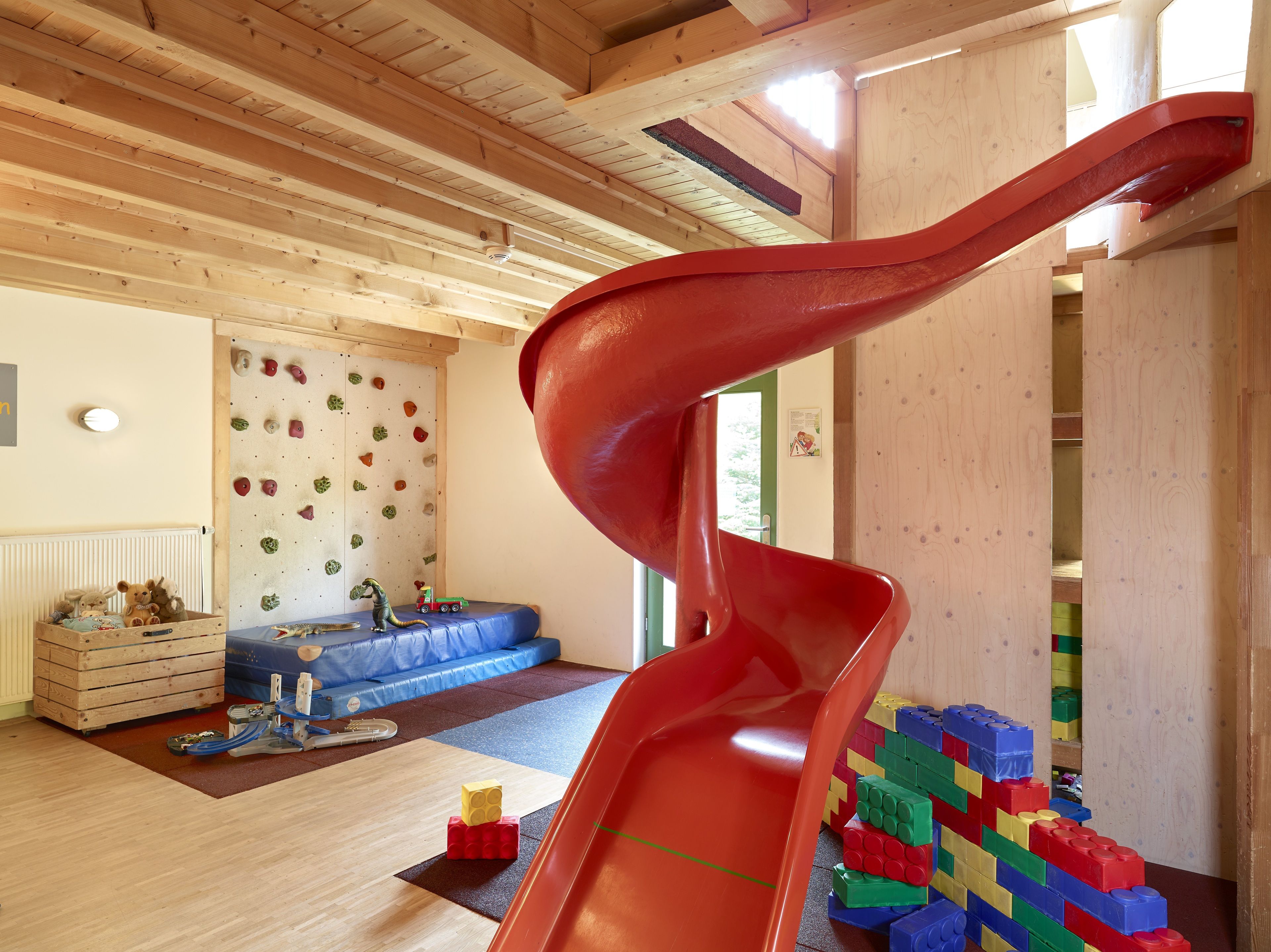 A room with a wooden ceiling, a blue sofa, a climbing wall, and a red slide.